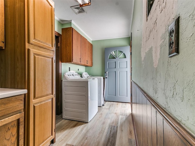 clothes washing area with ornamental molding, washer and clothes dryer, cabinets, and light hardwood / wood-style flooring