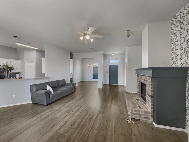 living room with wood-type flooring, ceiling fan with notable chandelier, and a brick fireplace