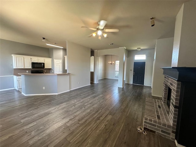 unfurnished living room with ceiling fan with notable chandelier, dark hardwood / wood-style flooring, and a brick fireplace