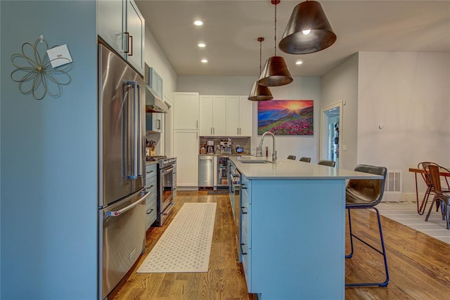 kitchen with white cabinets, sink, decorative light fixtures, light hardwood / wood-style floors, and stainless steel appliances