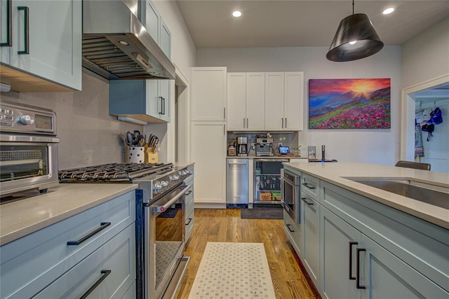 kitchen featuring stainless steel appliances, pendant lighting, white cabinets, exhaust hood, and light wood-type flooring