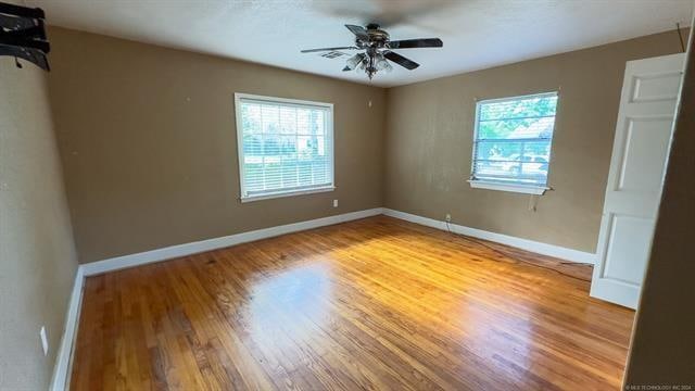 unfurnished bedroom featuring ceiling fan, wood-type flooring, and multiple windows