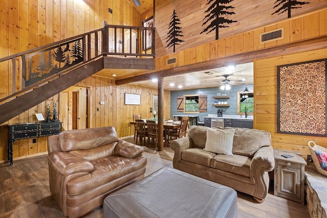 living room featuring a towering ceiling, ceiling fan, sink, hardwood / wood-style floors, and wood walls