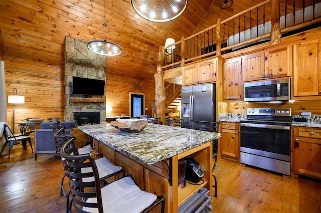 kitchen with a stone fireplace, light stone counters, high vaulted ceiling, and appliances with stainless steel finishes