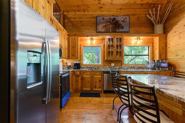 kitchen with appliances with stainless steel finishes, light stone counters, wood ceiling, light hardwood / wood-style flooring, and wood walls