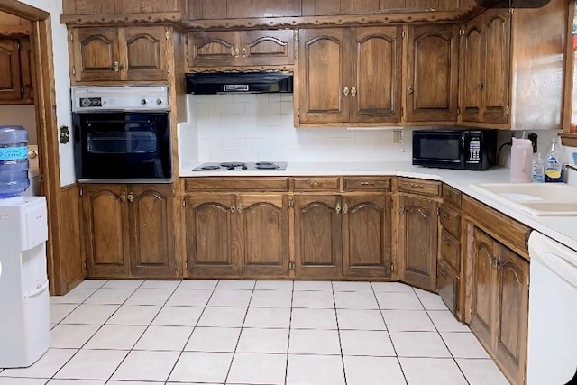 kitchen featuring sink, range hood, backsplash, light tile patterned floors, and black appliances