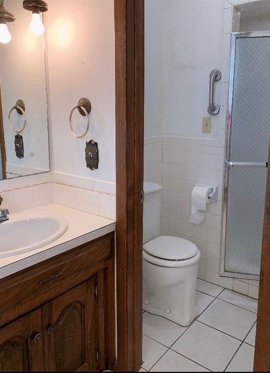 bathroom featuring tile patterned flooring, toilet, vanity, a shower with shower door, and tile walls