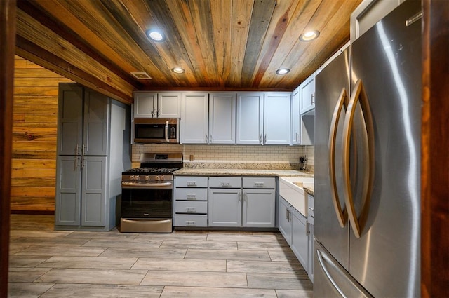 kitchen with light stone countertops, appliances with stainless steel finishes, gray cabinetry, and wooden ceiling