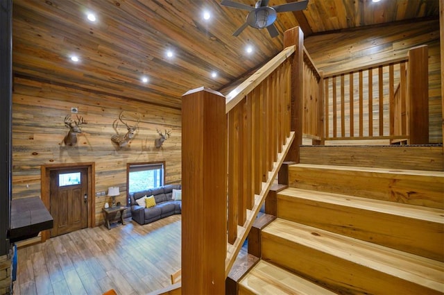 staircase featuring lofted ceiling, wood ceiling, ceiling fan, hardwood / wood-style floors, and wooden walls