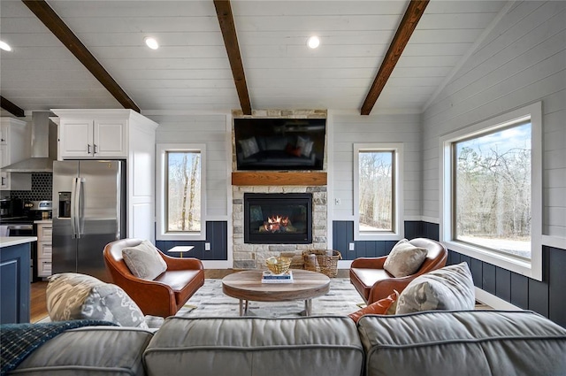 living room with a large fireplace, vaulted ceiling with beams, a wealth of natural light, and hardwood / wood-style floors