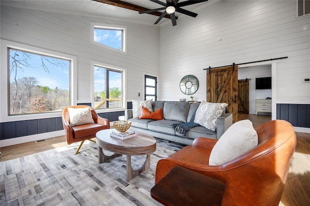 living room featuring light hardwood / wood-style floors, ceiling fan, a barn door, high vaulted ceiling, and beam ceiling