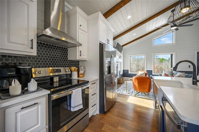 kitchen with appliances with stainless steel finishes, white cabinetry, vaulted ceiling with beams, and wall chimney range hood