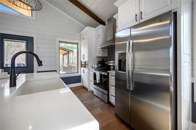 kitchen featuring sink, white cabinetry, lofted ceiling with beams, wall chimney range hood, and stainless steel appliances