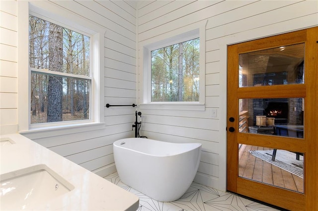 bathroom with a tub, wood walls, a fireplace, and vanity