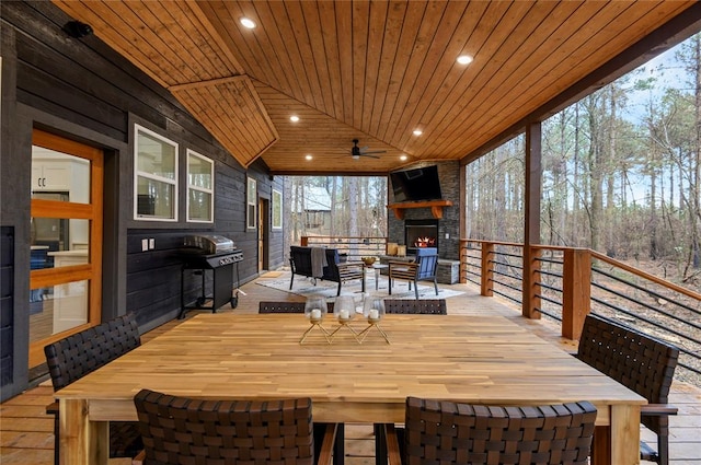 wooden terrace featuring an outdoor stone fireplace, a grill, and ceiling fan