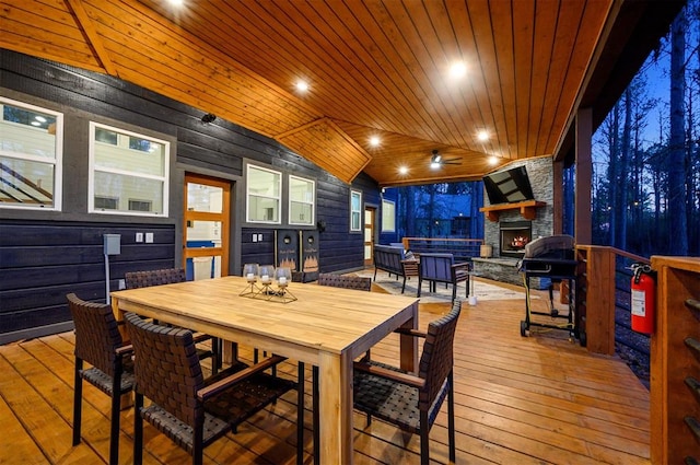 dining room with an outdoor stone fireplace, wooden ceiling, wooden walls, and vaulted ceiling