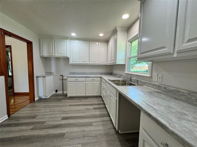 kitchen with a textured ceiling, light wood-type flooring, white cabinetry, and sink