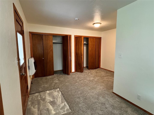 unfurnished bedroom with heating unit, carpet, two closets, and a textured ceiling