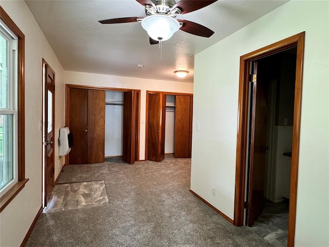 unfurnished bedroom with carpet, heating unit, ceiling fan, and multiple closets