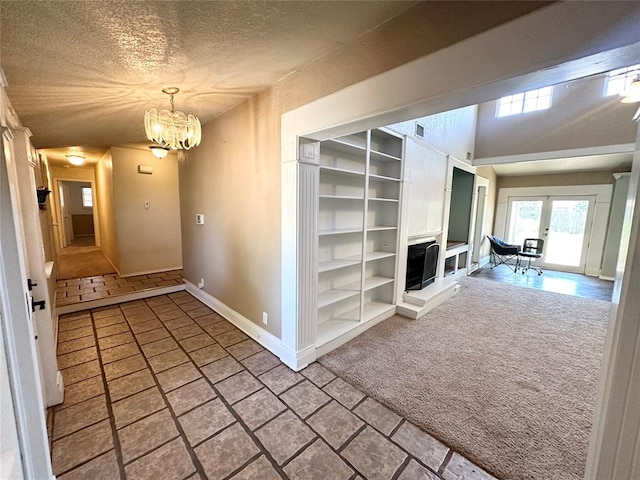 hallway with carpet, french doors, a textured ceiling, and an inviting chandelier