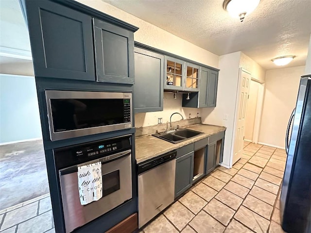 kitchen with appliances with stainless steel finishes, a textured ceiling, gray cabinets, and sink