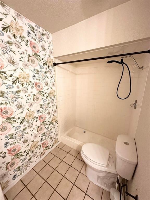 bathroom featuring tile patterned floors, tiled shower, toilet, and a textured ceiling