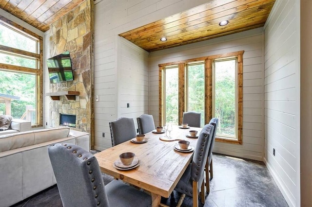 dining area with a fireplace, wooden ceiling, and wooden walls