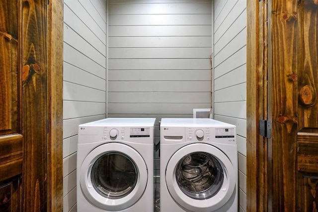 washroom featuring washer and clothes dryer and wood walls