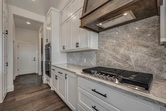 kitchen featuring dark wood-type flooring, light stone counters, stainless steel gas stovetop, decorative backsplash, and white cabinets