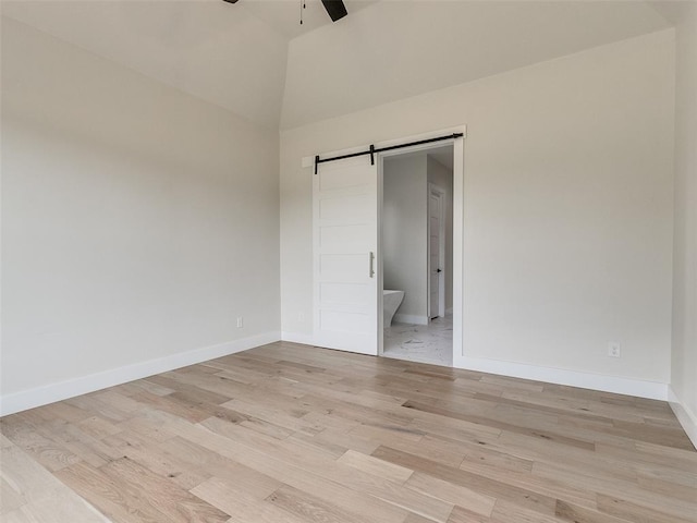 unfurnished bedroom with light wood-type flooring, a towering ceiling, ensuite bathroom, ceiling fan, and a barn door