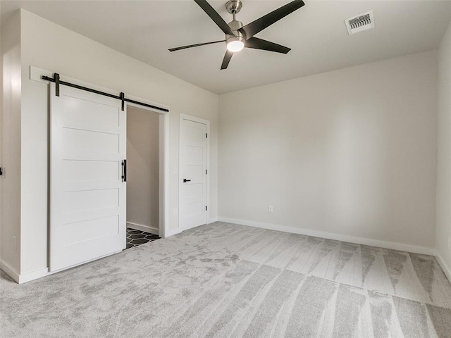 unfurnished bedroom with a closet, a barn door, carpet floors, and ceiling fan