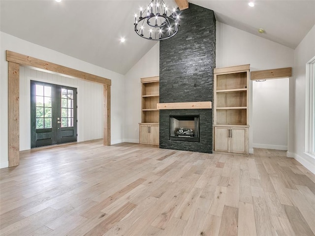 unfurnished living room with french doors, a stone fireplace, high vaulted ceiling, a chandelier, and light hardwood / wood-style floors