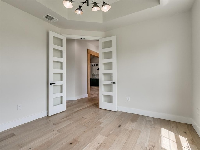 empty room with a notable chandelier, french doors, and light hardwood / wood-style flooring