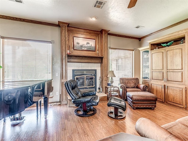 living room featuring a tiled fireplace, ornamental molding, a textured ceiling, and light wood-type flooring