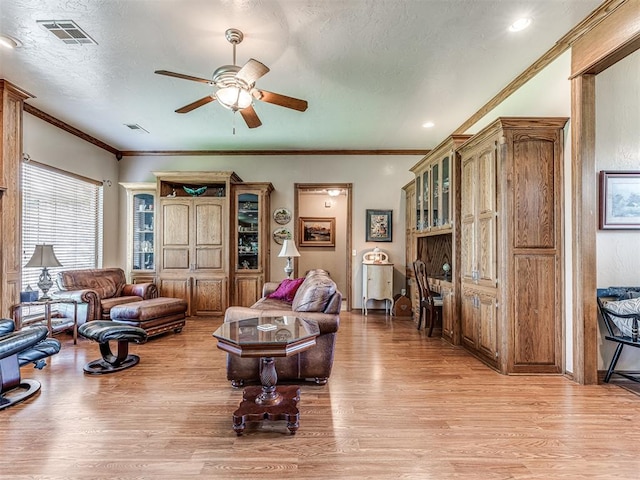 living room featuring ceiling fan, light hardwood / wood-style flooring, a textured ceiling, and ornamental molding