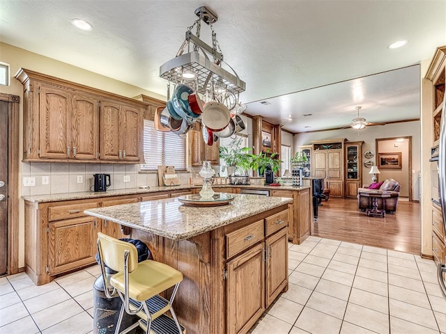 kitchen featuring ceiling fan, a center island, a kitchen breakfast bar, light stone counters, and light tile patterned flooring