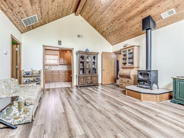 living room featuring beam ceiling, a wood stove, sink, light hardwood / wood-style flooring, and high vaulted ceiling