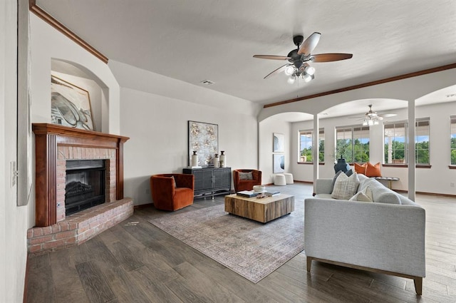 living room with a fireplace, dark hardwood / wood-style floors, ceiling fan, and ornamental molding