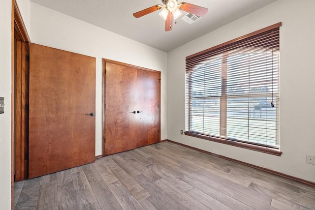 unfurnished bedroom featuring hardwood / wood-style flooring, ceiling fan, and multiple windows