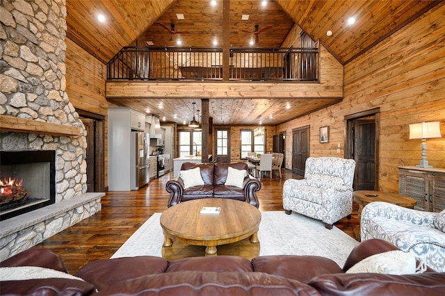 living room featuring high vaulted ceiling, wood ceiling, a stone fireplace, and wood walls