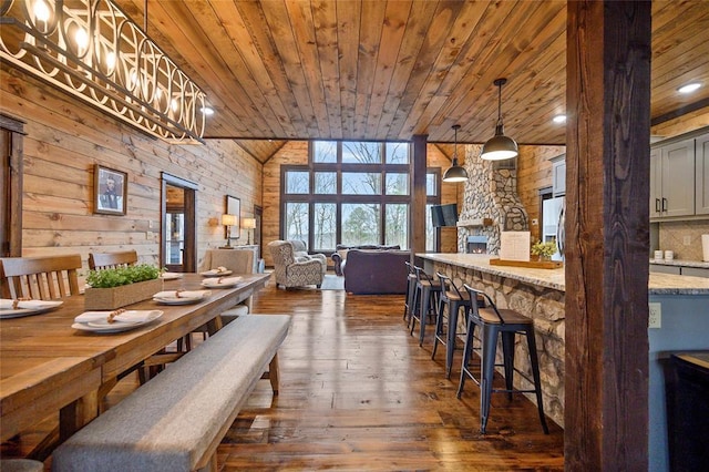 dining area featuring dark hardwood / wood-style floors, wood walls, wood ceiling, and a fireplace