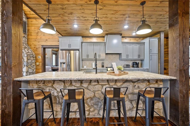 kitchen featuring a kitchen bar, wood ceiling, custom range hood, stainless steel fridge with ice dispenser, and hanging light fixtures