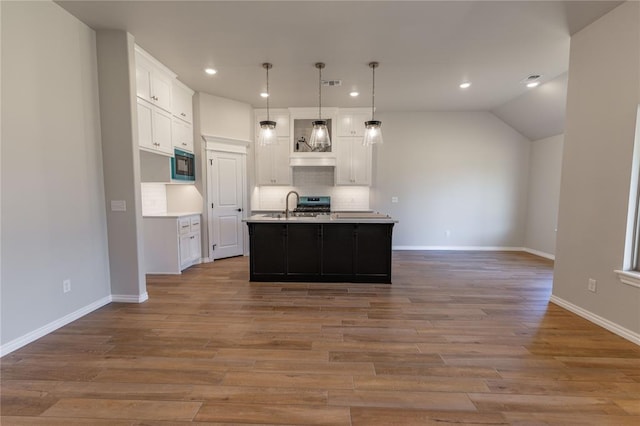 kitchen featuring white cabinetry, black microwave, pendant lighting, light hardwood / wood-style floors, and a kitchen island with sink