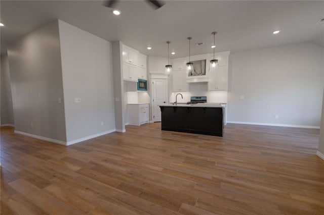 kitchen with a center island with sink, white cabinets, hanging light fixtures, and light hardwood / wood-style flooring