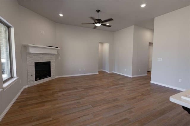 unfurnished living room with a stone fireplace, ceiling fan, and wood-type flooring