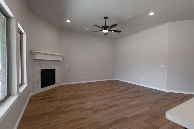 unfurnished living room with ceiling fan, a stone fireplace, and dark hardwood / wood-style flooring