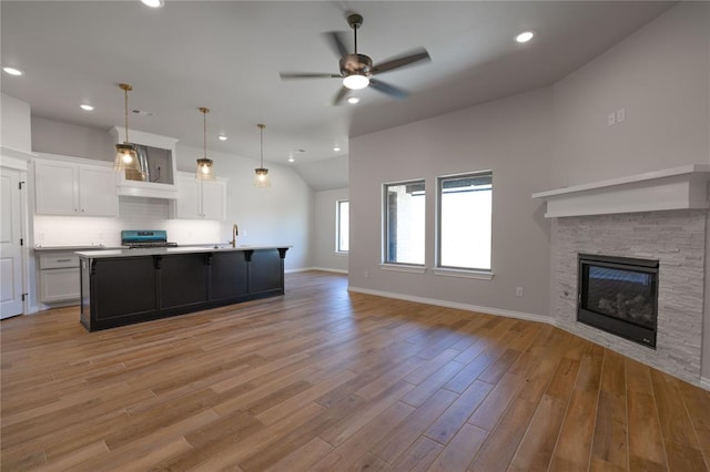 kitchen with white cabinetry, light hardwood / wood-style flooring, pendant lighting, a fireplace, and a center island with sink