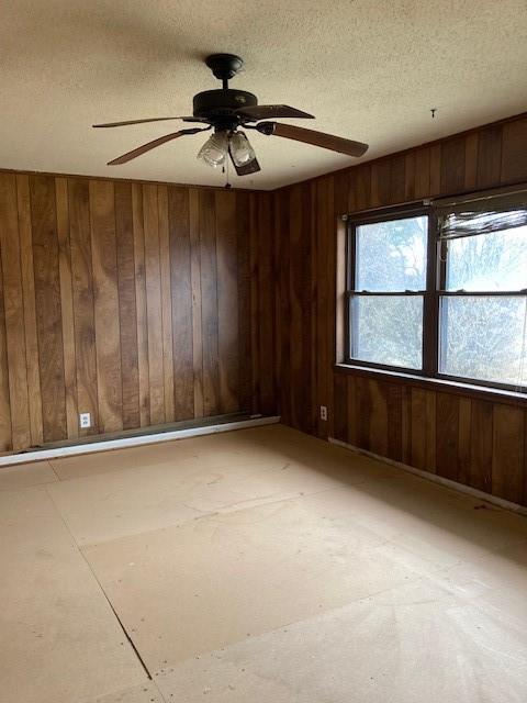 unfurnished room with a textured ceiling, ceiling fan, and wooden walls