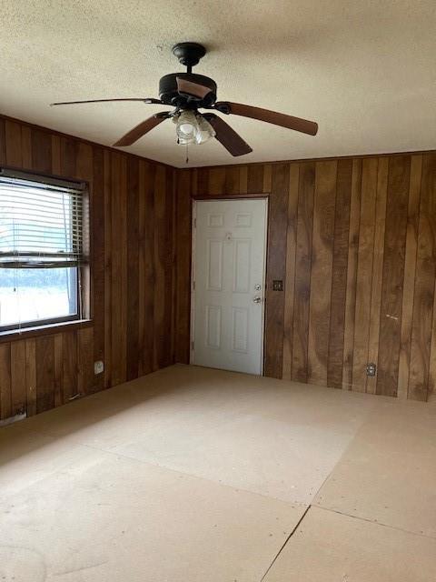 unfurnished room with ceiling fan, wooden walls, and a textured ceiling