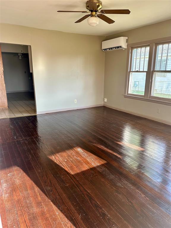 empty room featuring hardwood / wood-style flooring, ceiling fan, and a wall unit AC